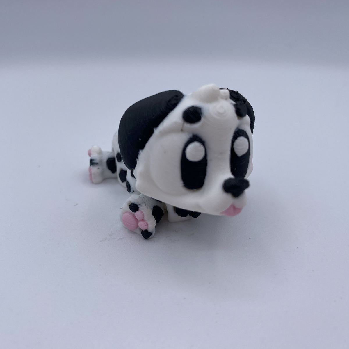 A small black and white spotted dog figurine with pink paw pads, photographed on a plain light gray background.