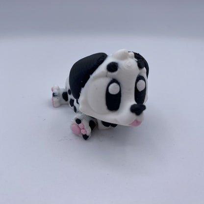 A small black and white spotted dog figurine with pink paw pads, photographed on a plain light gray background.