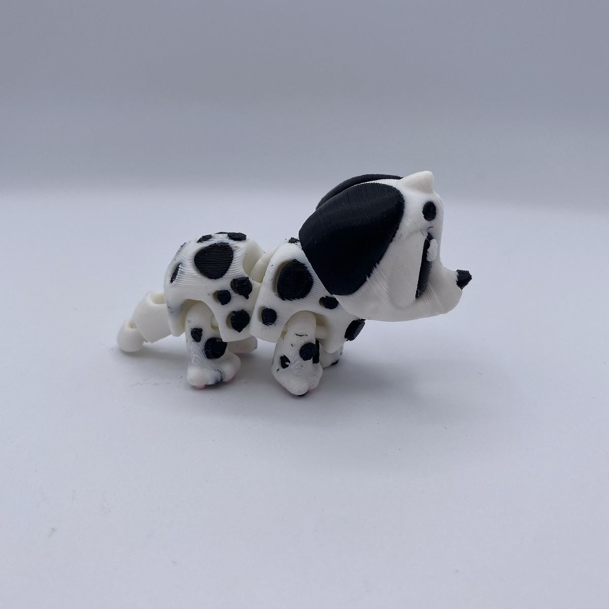 A small black and white spotted dog figurine, resembling a Dalmatian puppy, standing on a plain light gray background.