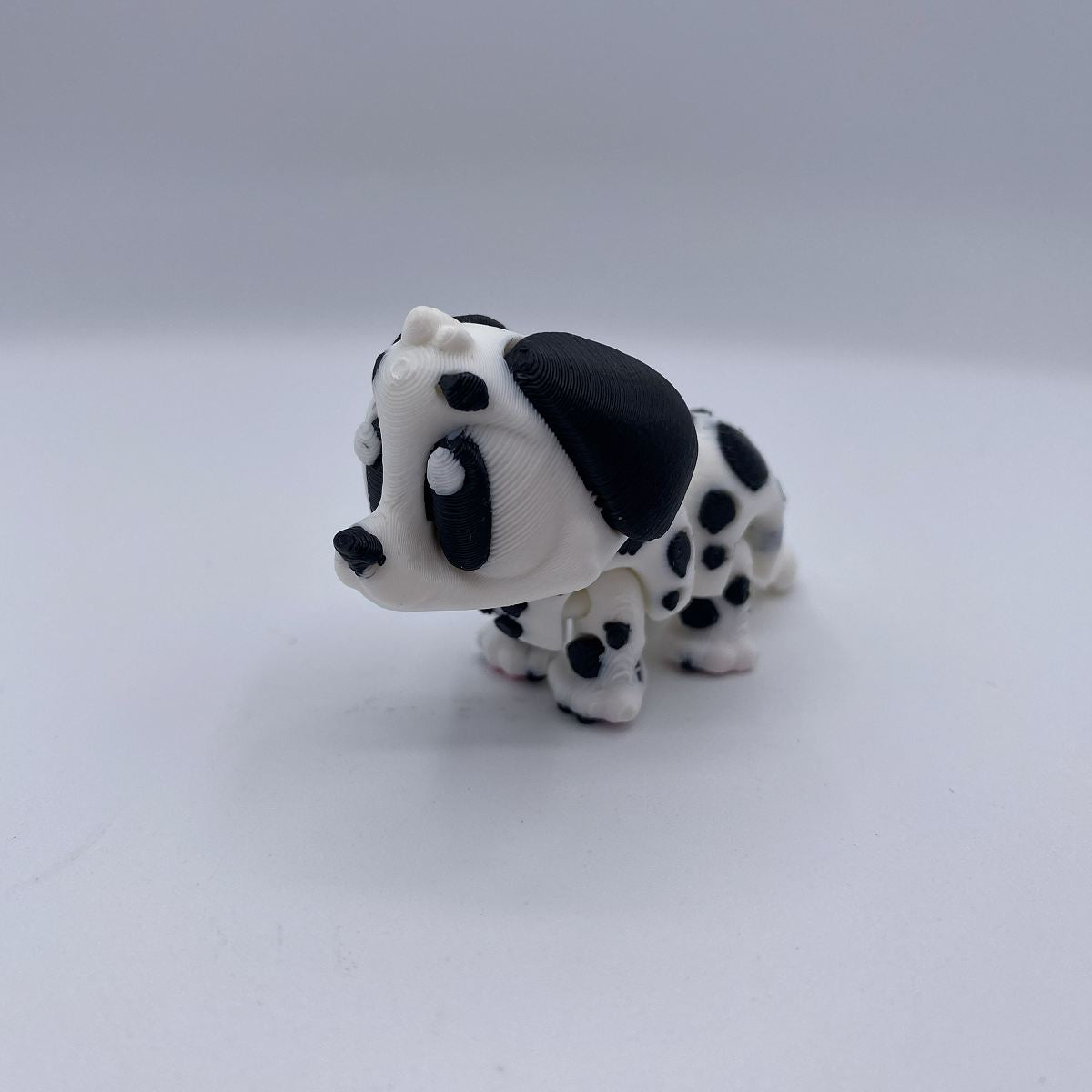 A small black and white spotted dog figurine, resembling a dalmatian puppy, photographed on a plain light gray background.