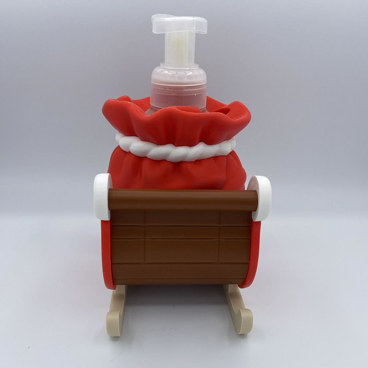A novelty Christmas-themed foam bottle shaped like a Santa sack in a wooden sleigh, photographed against a neutral gray studio background.